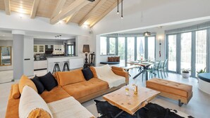 A modern living room with a sofa, ottoman, and coffee table, a dining area with chairs and a table, and a kitchen in the background. - Villa Tolena by Marilena Pagkrati (Corfu)