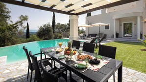 A dining area with a pool view, outdoor seating, and a well-maintained lawn. - Villa Tolena by Marilena Pagkrati (Corfu)