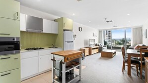 A modern kitchen with a stove, oven, and refrigerator, a dining area with a wooden table and chairs, and a living room with a sofa and a TV.