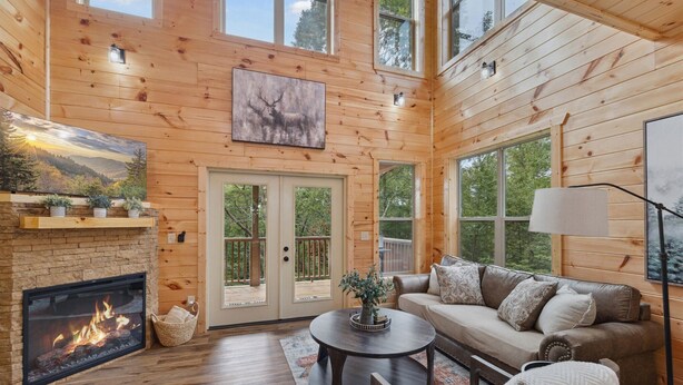 Ein gemütliches Blockhäuschen im Inneren mit Kamin, Holzwänden, einer Couch und einem großen Fenster.