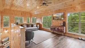 Ein Holzblock-Interieur mit einer Couch, einem Esstisch und einem großen Fenster mit Blick auf den Wald.