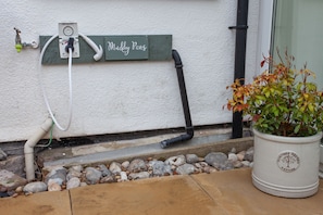 Un espace aménagé en jardin, avec un pot de fleurs, un panneau indiquant « Muddy Paws » et un système de tuyauterie d’alimentation en eau.