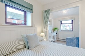 Un dormitorio con cama, escritorio, silla y ventana con cortinas.
