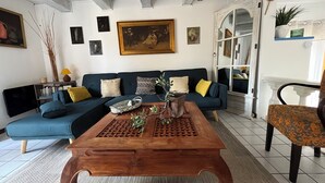 A living room with a dark blue sofa, a wooden coffee table, and a variety of decorative items including a painting, a plant, and a lamp. - La Maison Près de la Fontaine (Talairan)