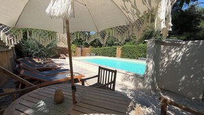 A poolside area with lounge chairs, a wooden deck, and an umbrella providing shade. - La Maison Près de la Fontaine (Talairan)