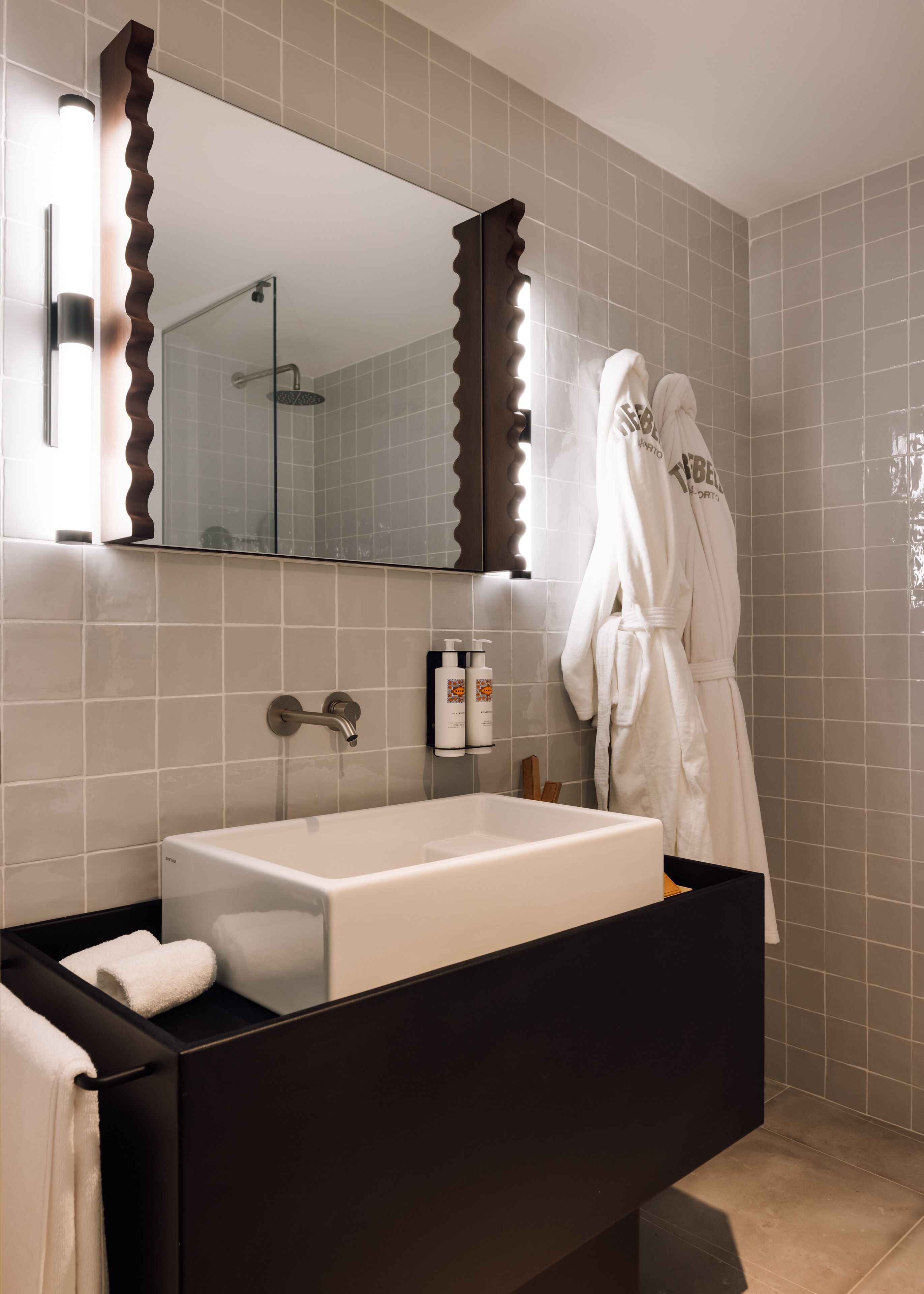 A modern bathroom with a large mirror, a black vanity, a white sink, and two white towels on the counter.