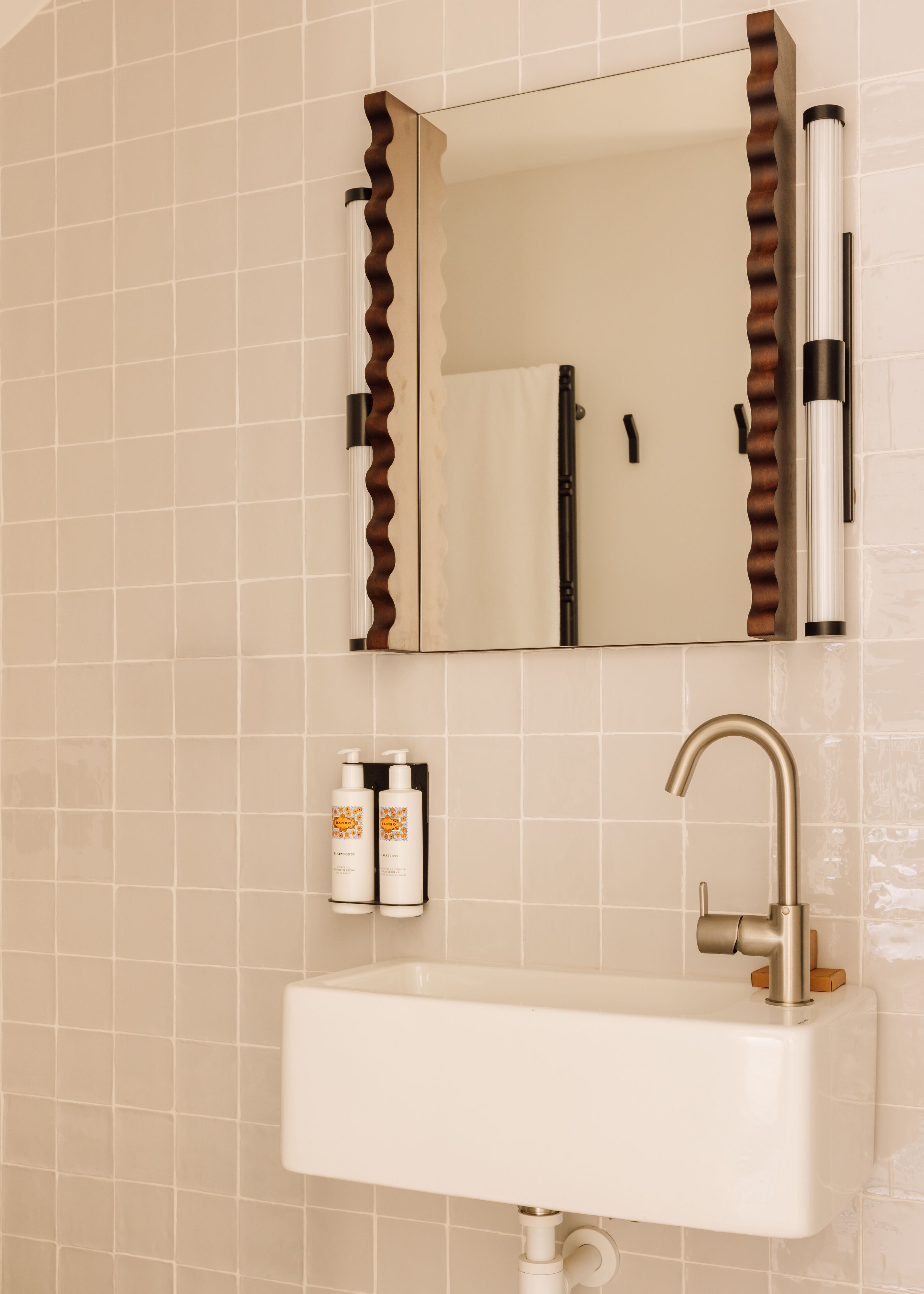 A bathroom with a white sink, a mirror with a wavy frame, and two bottles of shampoo.