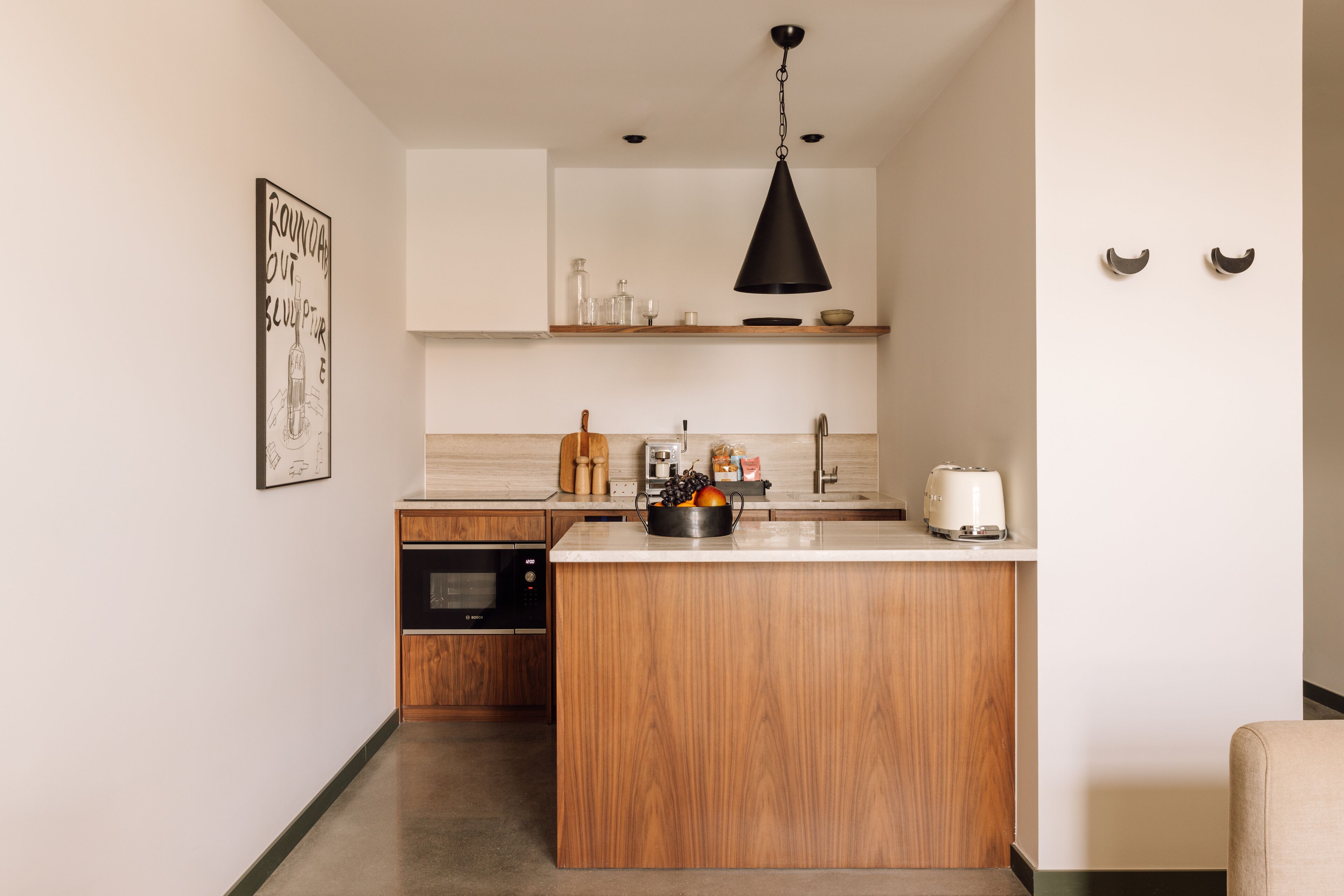 A modern kitchen with a wooden island, black pendant light, and a framed artwork on the wall.