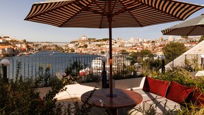 A terrace with a table and chairs, a large striped umbrella, and a view of a cityscape and water. - The Rebello Hotel & Spa (Vila Nova de Gaia)