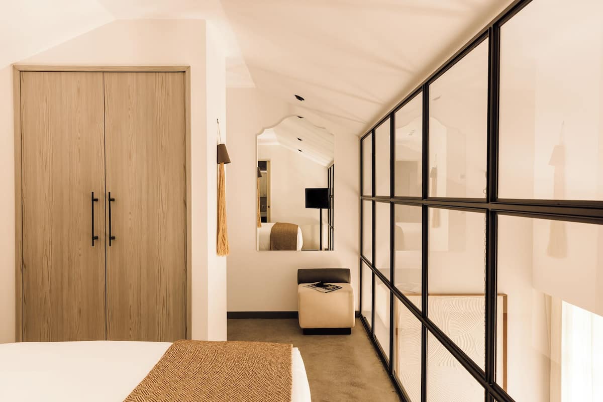 A bedroom with a bed, a wardrobe, a small seating area, and a large window.