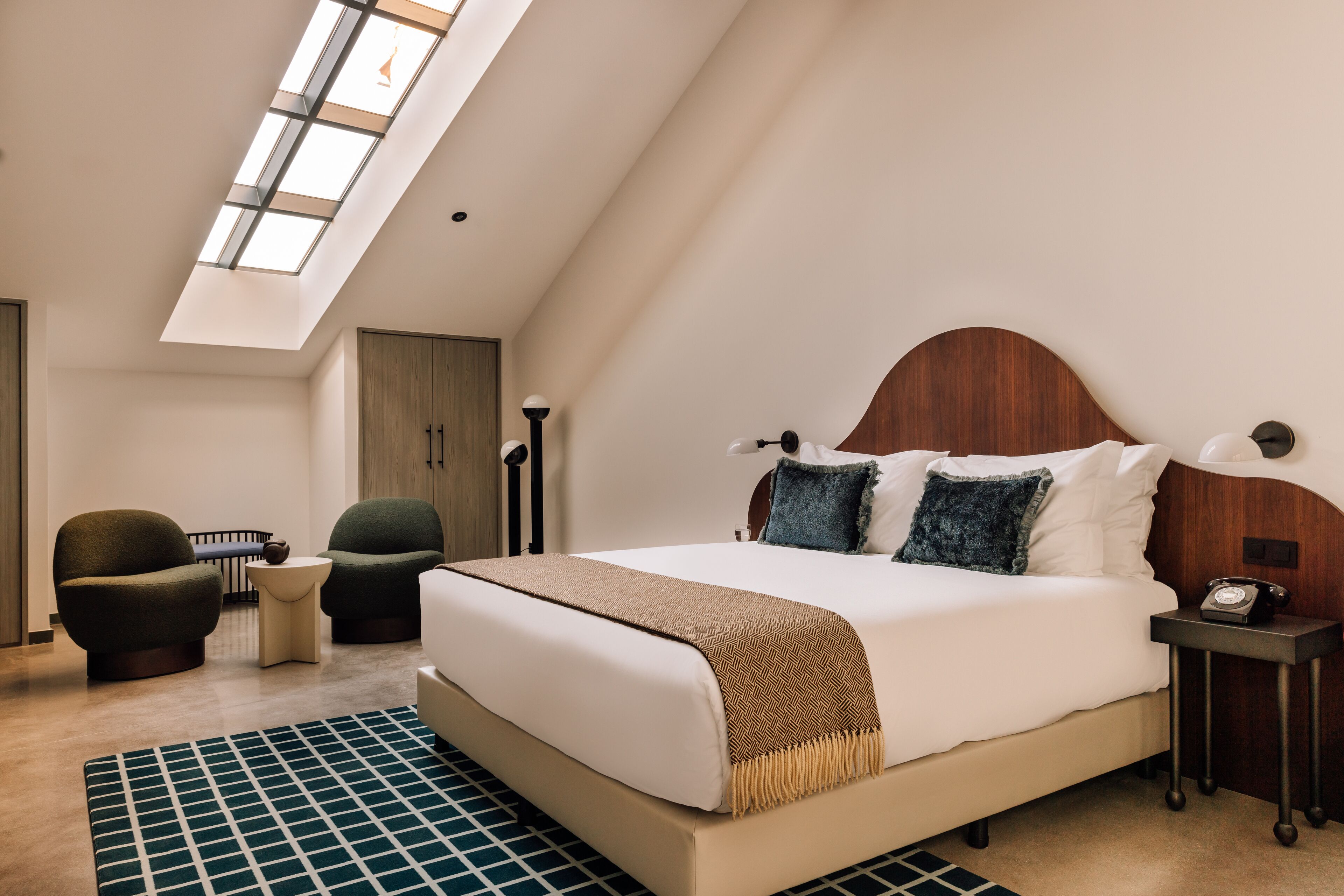 A modern bedroom with a large bed, two armchairs, a small table, and a nightstand.