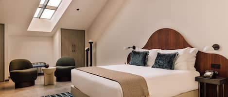 A modern bedroom with a large bed, two armchairs, a small table, and a nightstand.