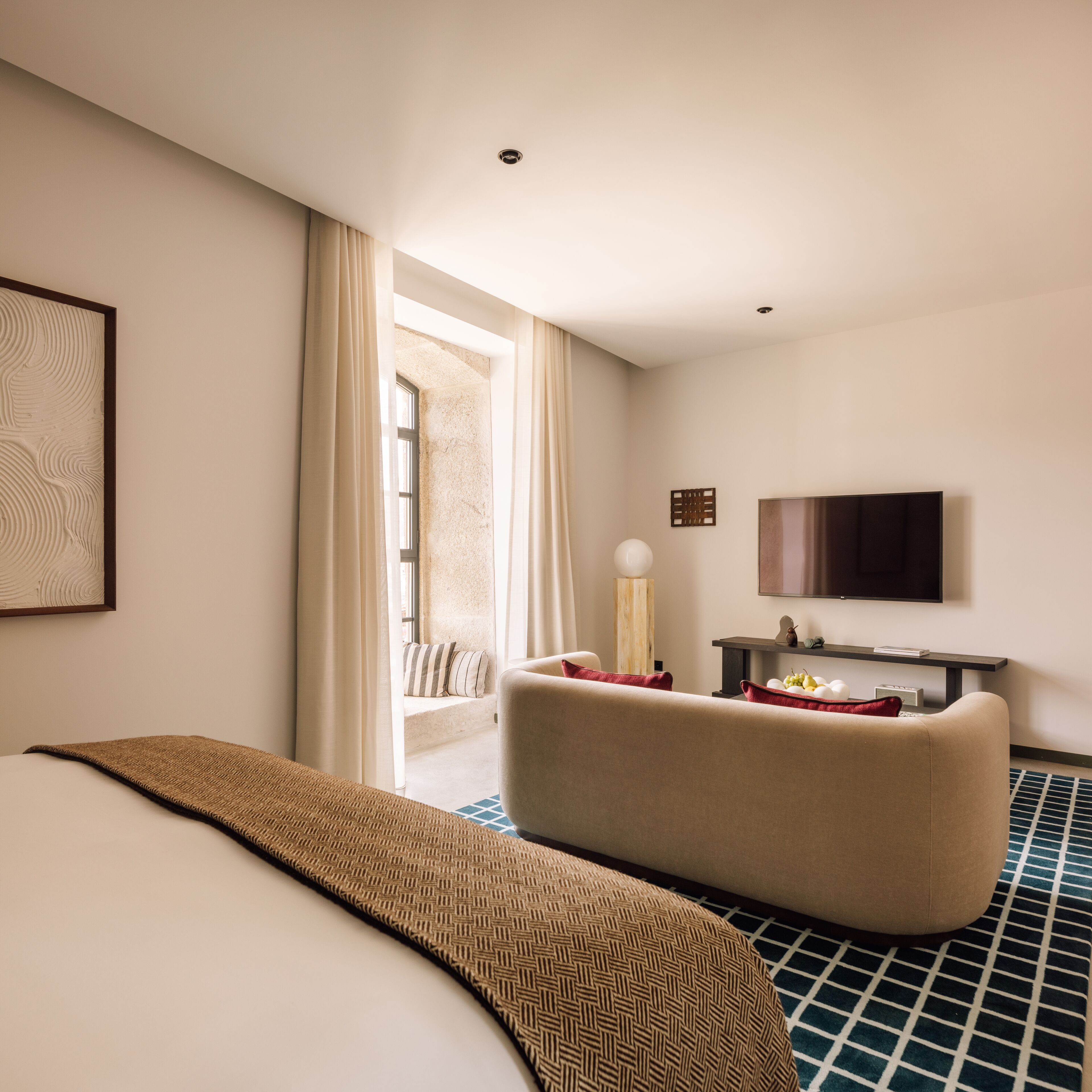 A hotel room with a bed, a sofa, a TV, and a window with curtains.