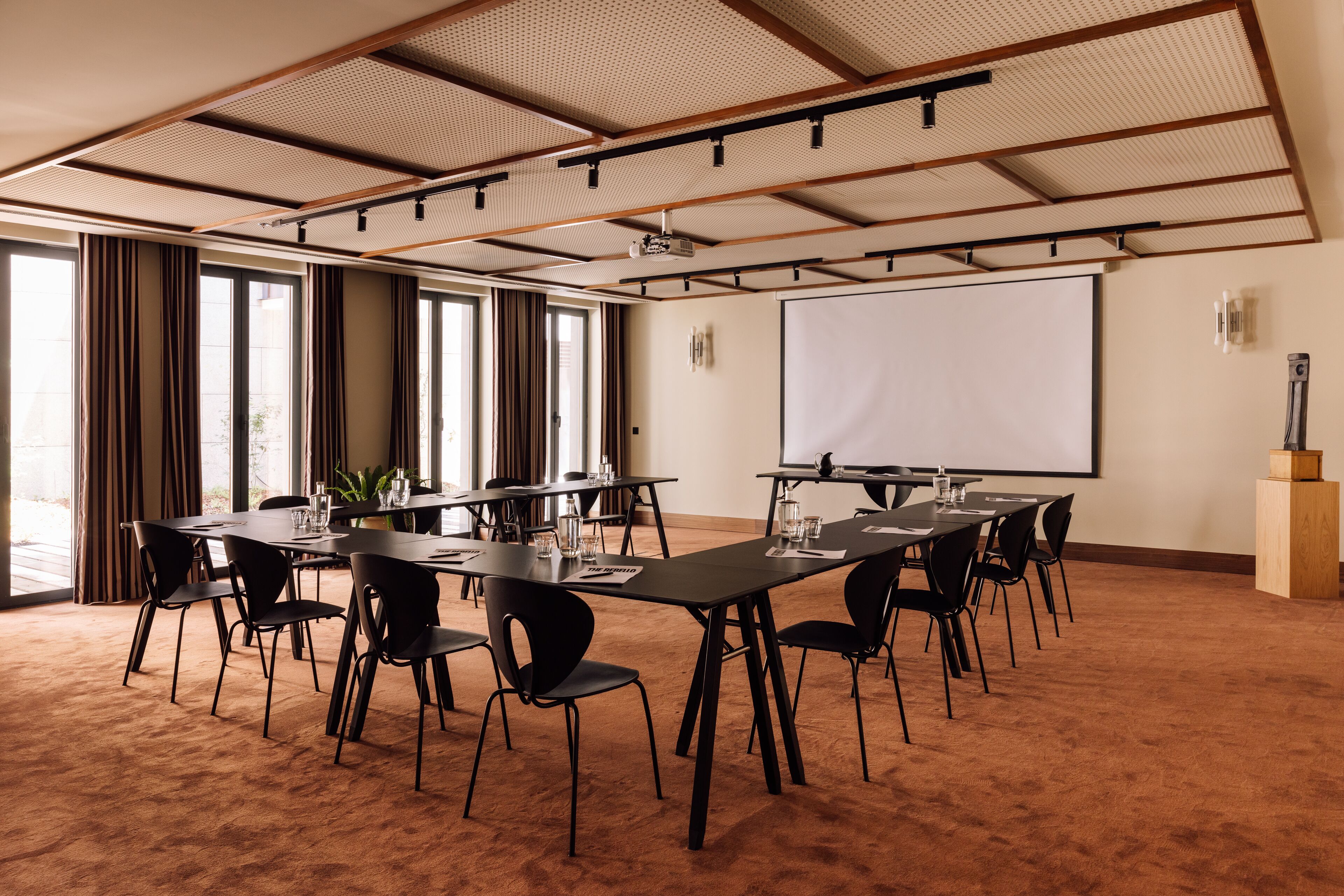 Ein Konferenzraum mit einem großen Tisch, Stühlen, einer Projektionsleinwand und Teppichboden.