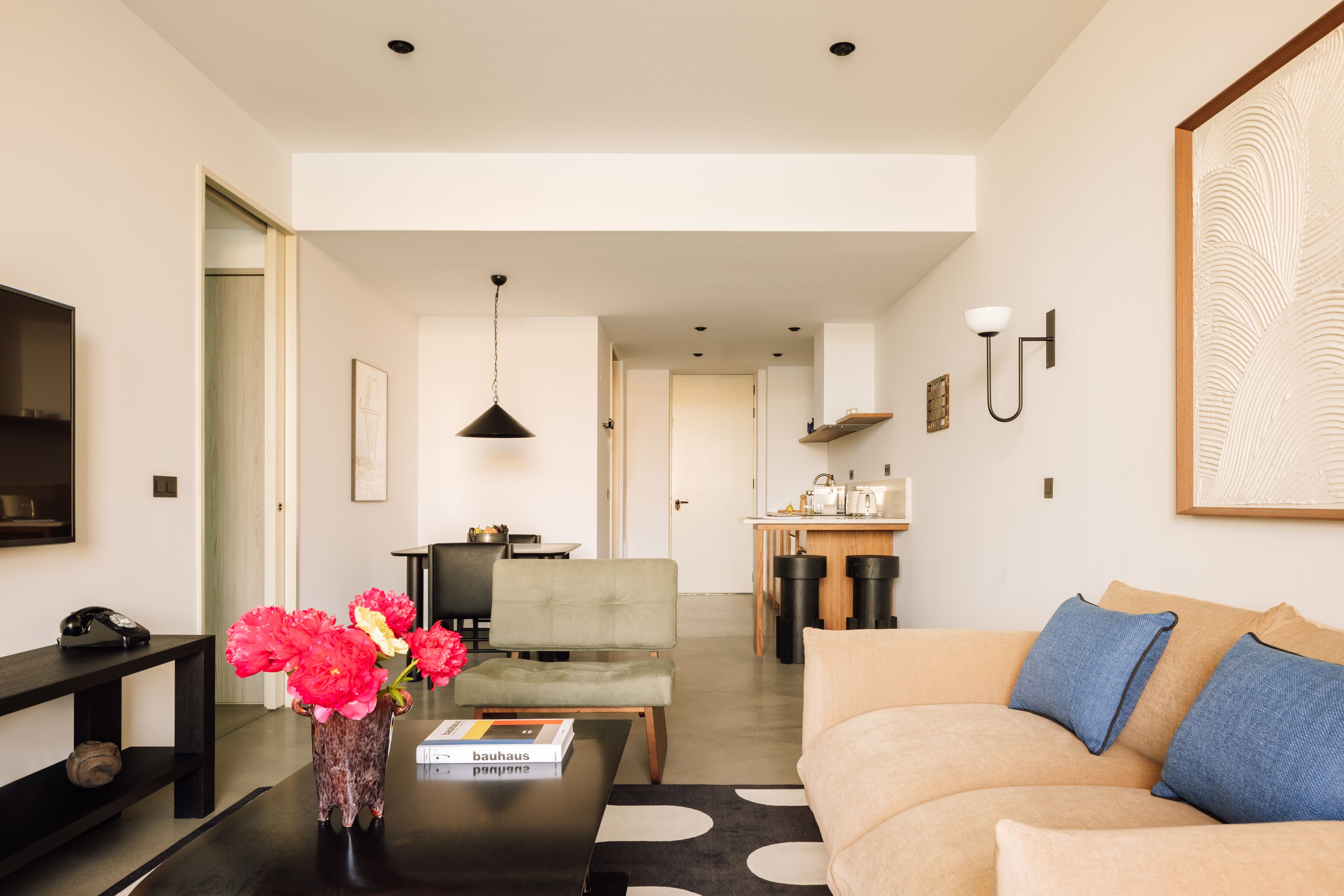 A modern living room with a sofa, a coffee table, a vase with flowers, a bookshelf, and a television.