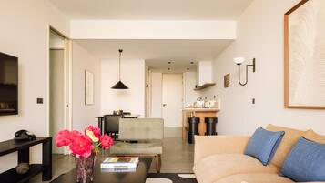 A modern living room with a sofa, a coffee table, a vase with flowers, a bookshelf, and a television.