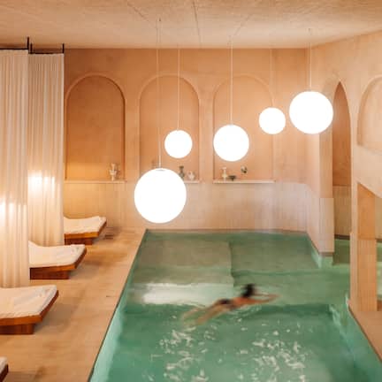 A spa room with a large pool, wooden loungers, and a person swimming.