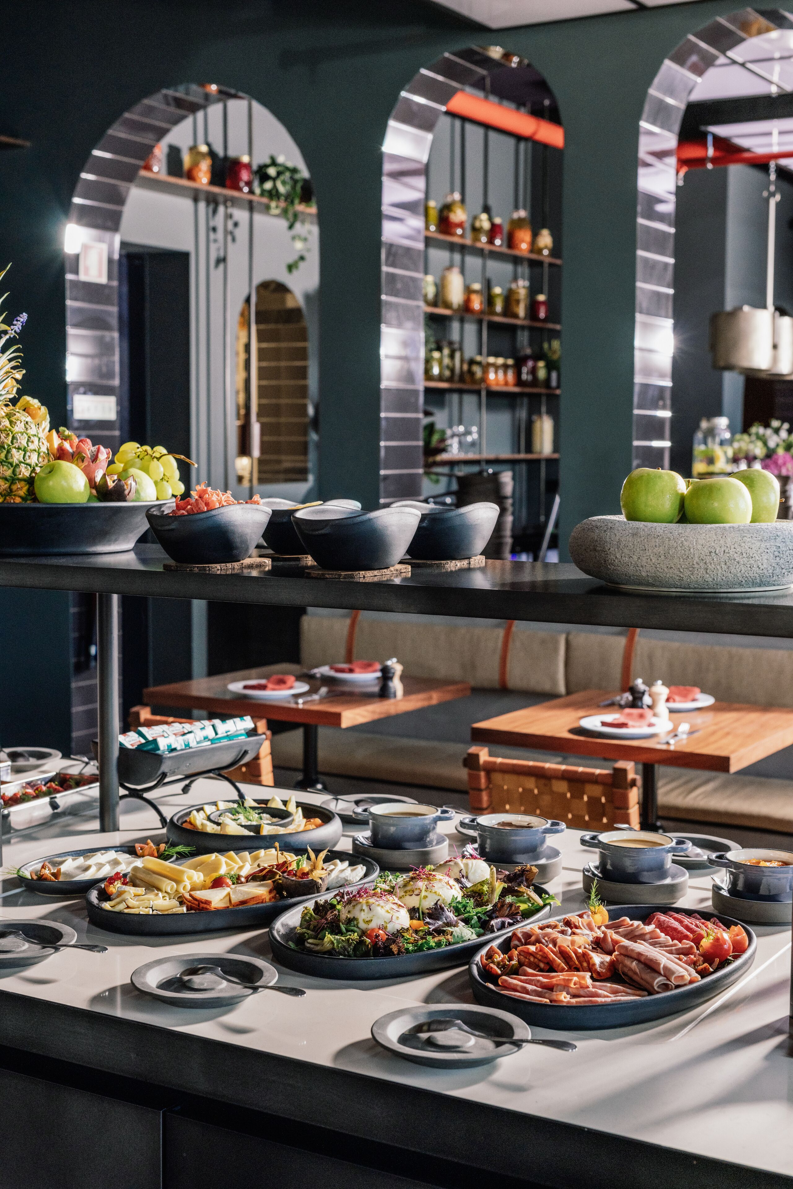 A buffet setup with various dishes and bowls on a table, surrounded by seating and shelves with jars.