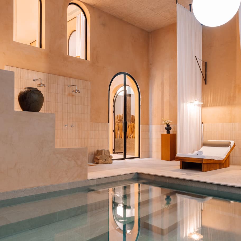 A modern indoor pool area with a clear pool, a lounge chair, and a large circular light fixture.