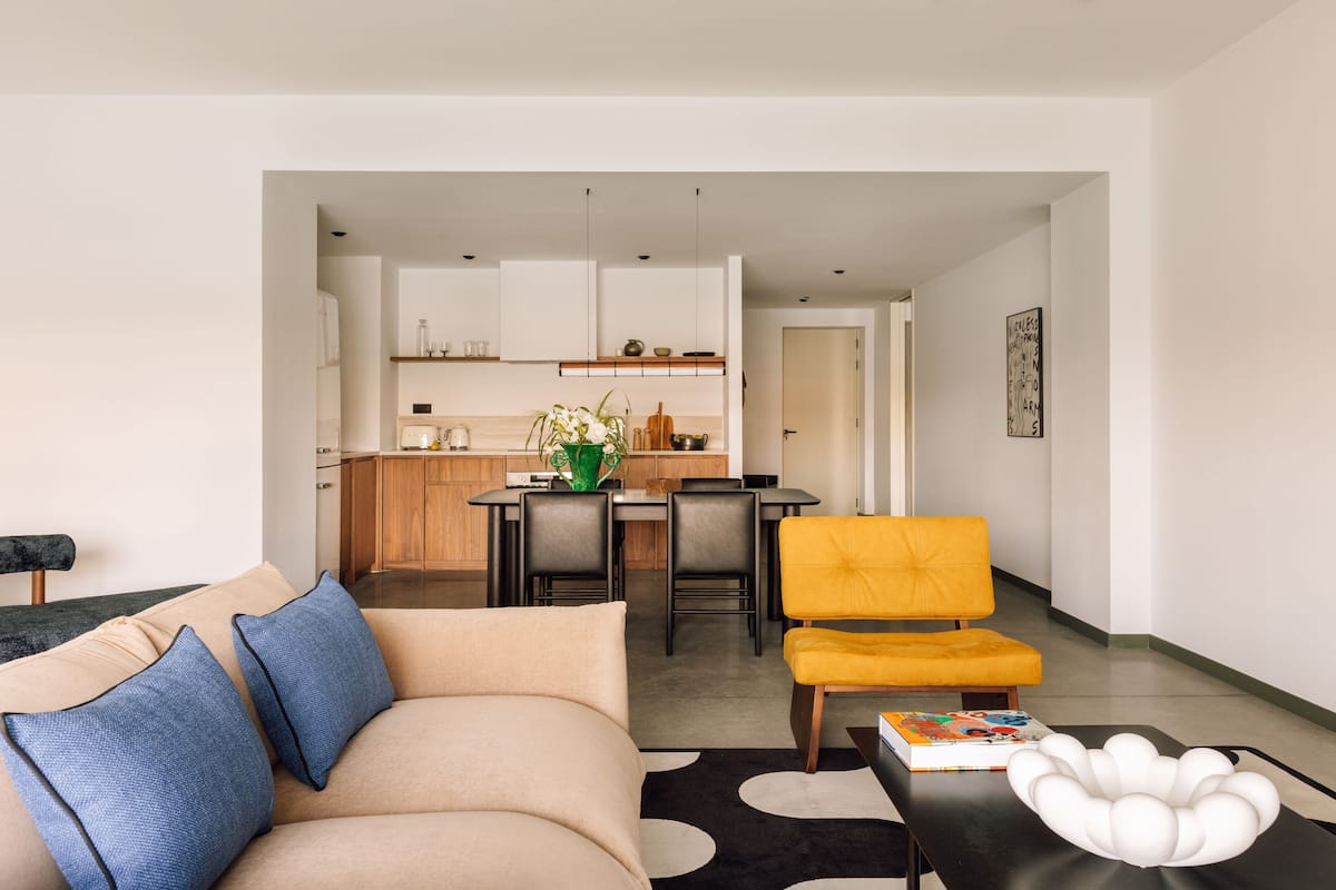 A modern living room with a sofa, a yellow armchair, and a dining area with a table and chairs.