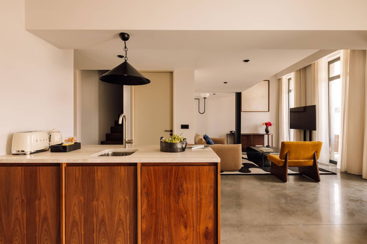 A modern kitchen with wooden cabinets, a built-in island, and a dining area with a yellow chair.