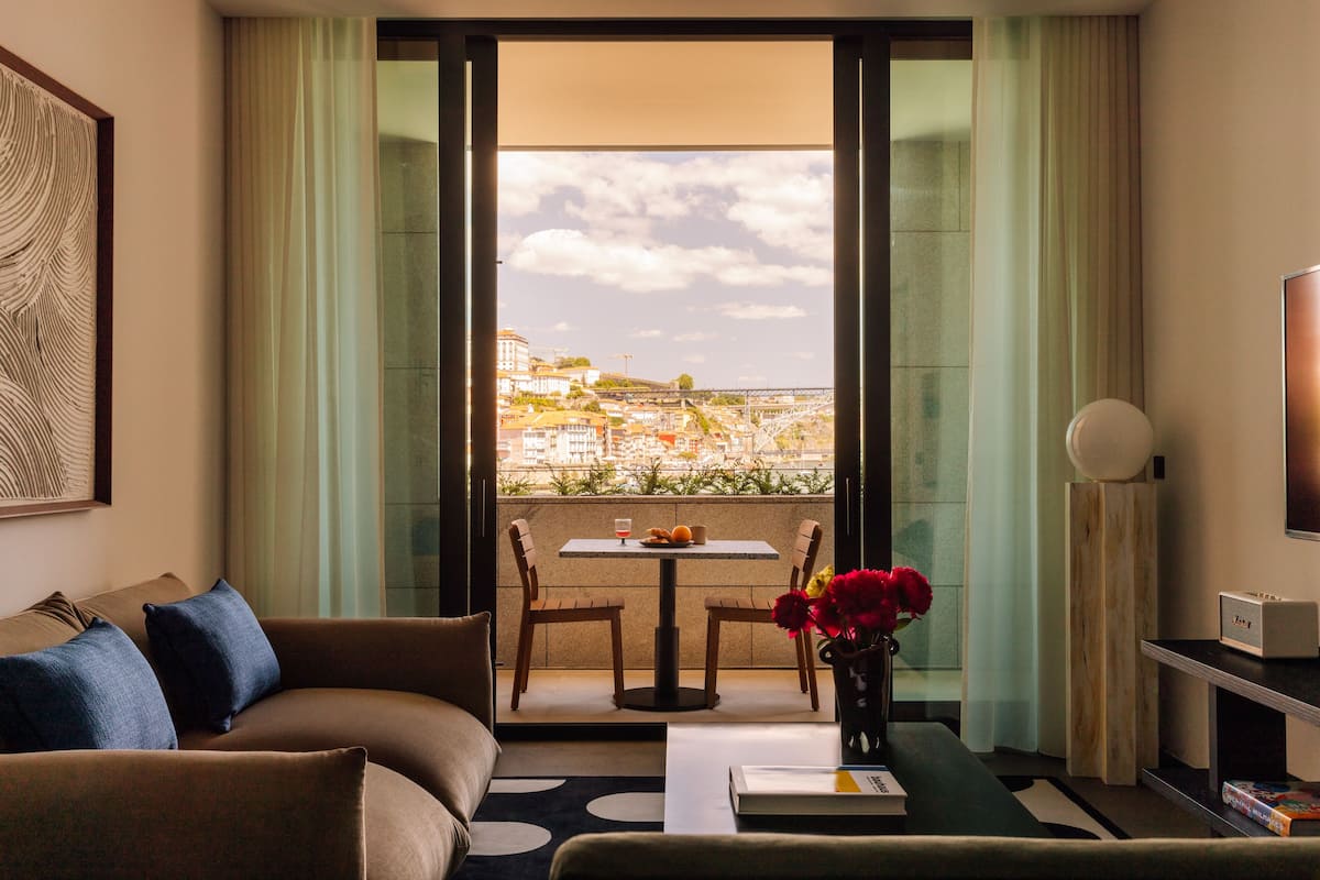 A hotel room with a balcony, a sofa, a table with fruit, and a vase with flowers.
