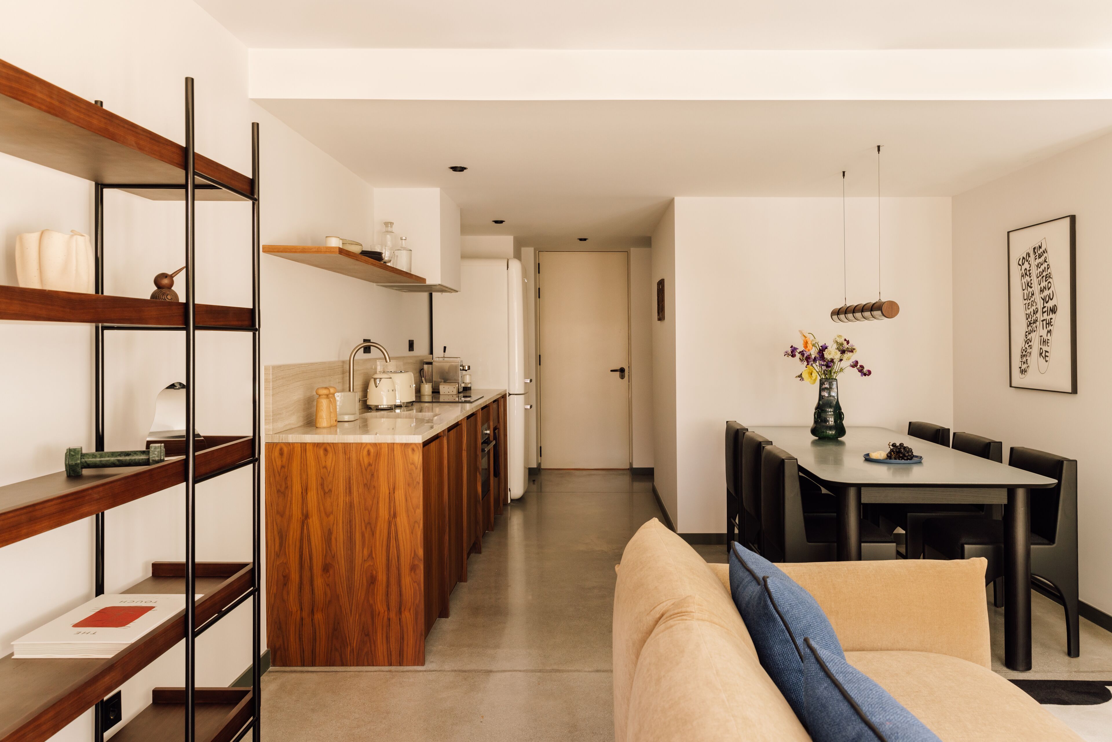 A modern kitchen with wooden shelves, a dining area with a table and chairs, and a cozy living space with a sofa.
