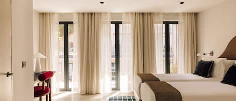 A hotel room with two beds, a red chair, a lamp, and a view of the outside through large windows.
