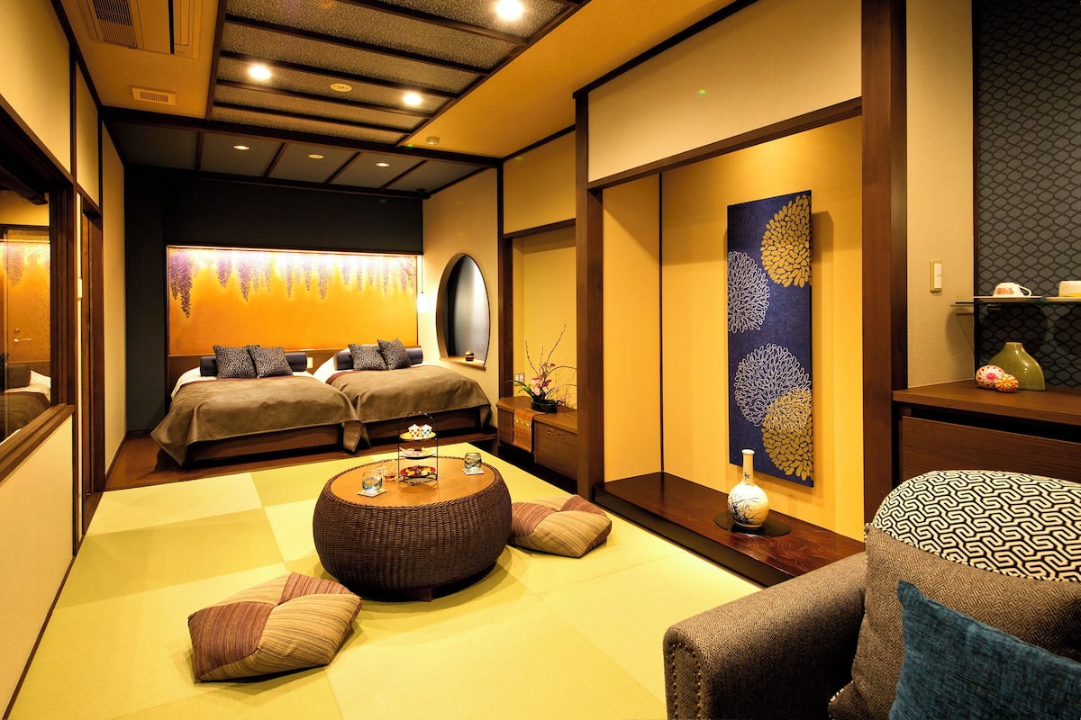 A traditional Japanese-style room with tatami flooring, two beds, a round wooden table, and a large decorative painting.
