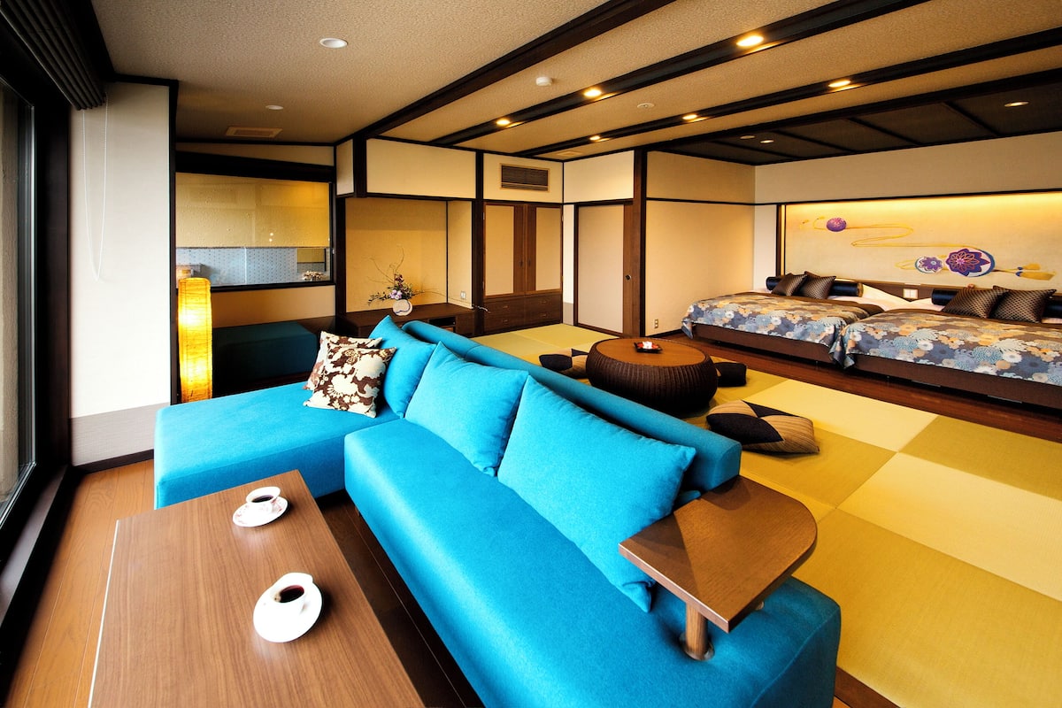 A modern hotel room with a blue sofa, a wooden coffee table, and a bed with floral bedding.