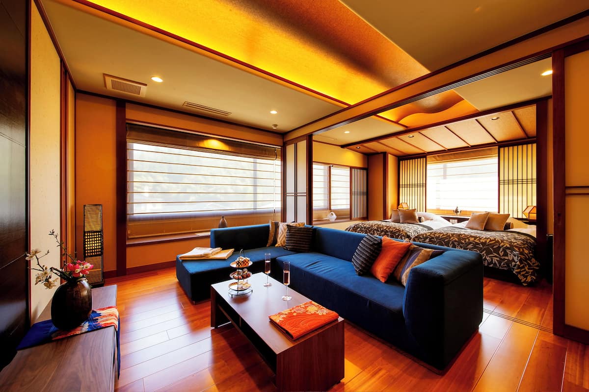 A modern hotel room with a large sofa, a bed with a patterned bedspread, and a wooden floor.