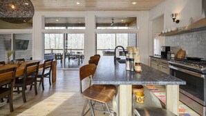 A modern kitchen with a central island, large windows, and a dining area with wooden furniture. - Pool, Pickleball & Basketball Court, Hot Tub, & Playset (Broken Bow)