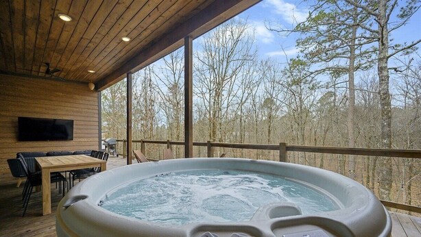 A hot tub on a wooden deck with a view of trees. - Pool, Pickleball & Basketball Court, Hot Tub, & Playset (Broken Bow)