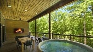 A wooden deck with a hot tub, a fire pit, and a dining area overlooking a forest. - Cabin w/ Heated Pool, Pickleball Court Access & Spacious Deck (Broken Bow)