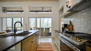 A modern kitchen with a large island, stainless steel appliances, and a view to a deck. - Cabin w/ Heated Pool, Pickleball Court Access & Spacious Deck (Broken Bow)