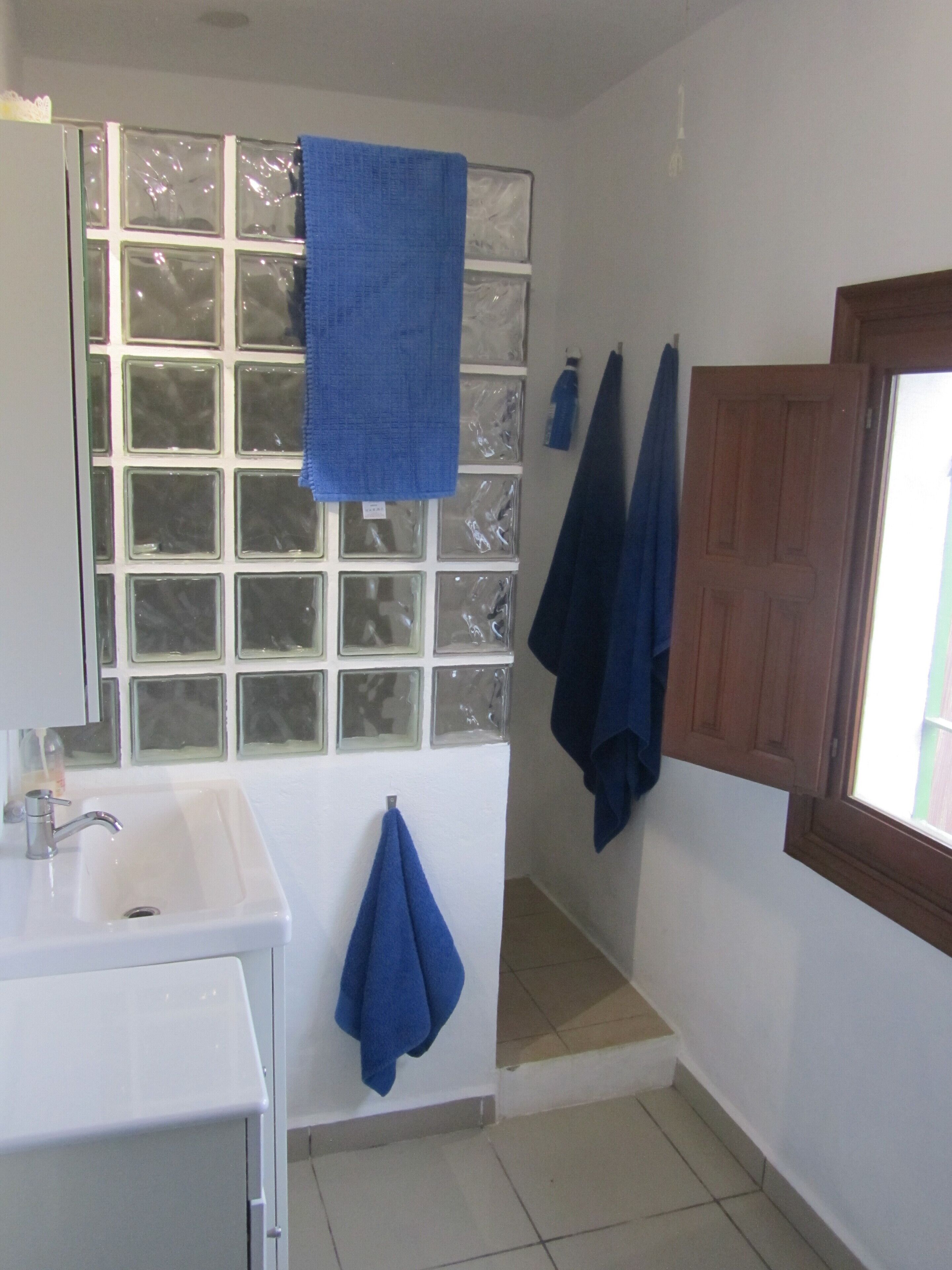 Un baño con un lavabo blanco, una ventana con vidrio esmerilado y dos toallas azules colgadas en la pared.
