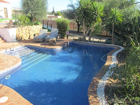 Una piscina al aire libre, sombrillas, sillones reclinables de piscina