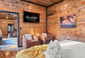 Ein Holzinterieur mit einem Fernseher, der 'TreeLine Vacation Rentals' anzeigt, und einem gerahmten Bild von einem Feld.
