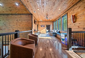 Un intérieur en bois avec un long couloir menant à une pièce dotée d’une cheminée, d’un bar et d’une enseigne indiquant « C’EST PARTI ! ».