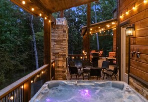 A hot tub on a wooden deck with stone pillars and string lights.
