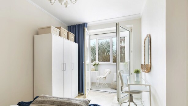 Un dormitorio con cama, armario, escritorio y silla. Hay una ventana y una puerta que da a un espacio exterior.