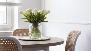 Una mesa redonda de madera con un florero de vidrio transparente que contiene tulipanes blancos, rodeada de sillas de mimbre.