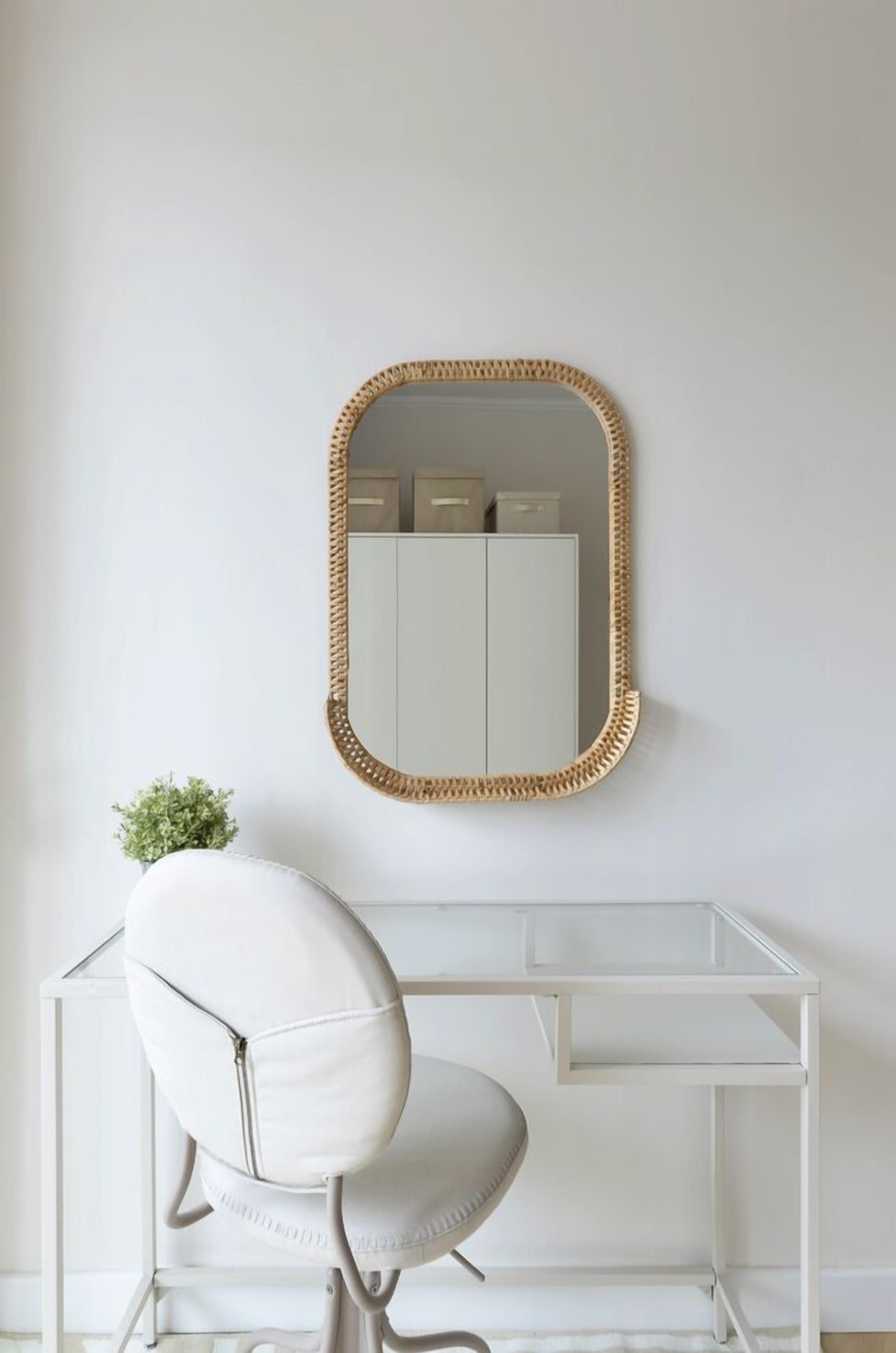 A white desk with a woven mirror above it, a white chair, and a small plant on the desk.