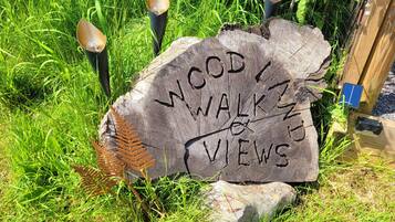 Ein Holzschild mit der Aufschrift 'WOOD WALKING ZONES', umgeben von Gras und Farnen.