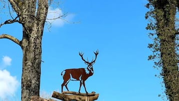 A deer sculpture on a log in a forested area with trees and a clear blue sky.
