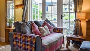 A cozy living room with a sofa, a wooden side table, and a view of the garden through large windows.