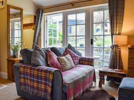 A cozy living room with a sofa, a wooden side table, and a view of the garden through large windows.
