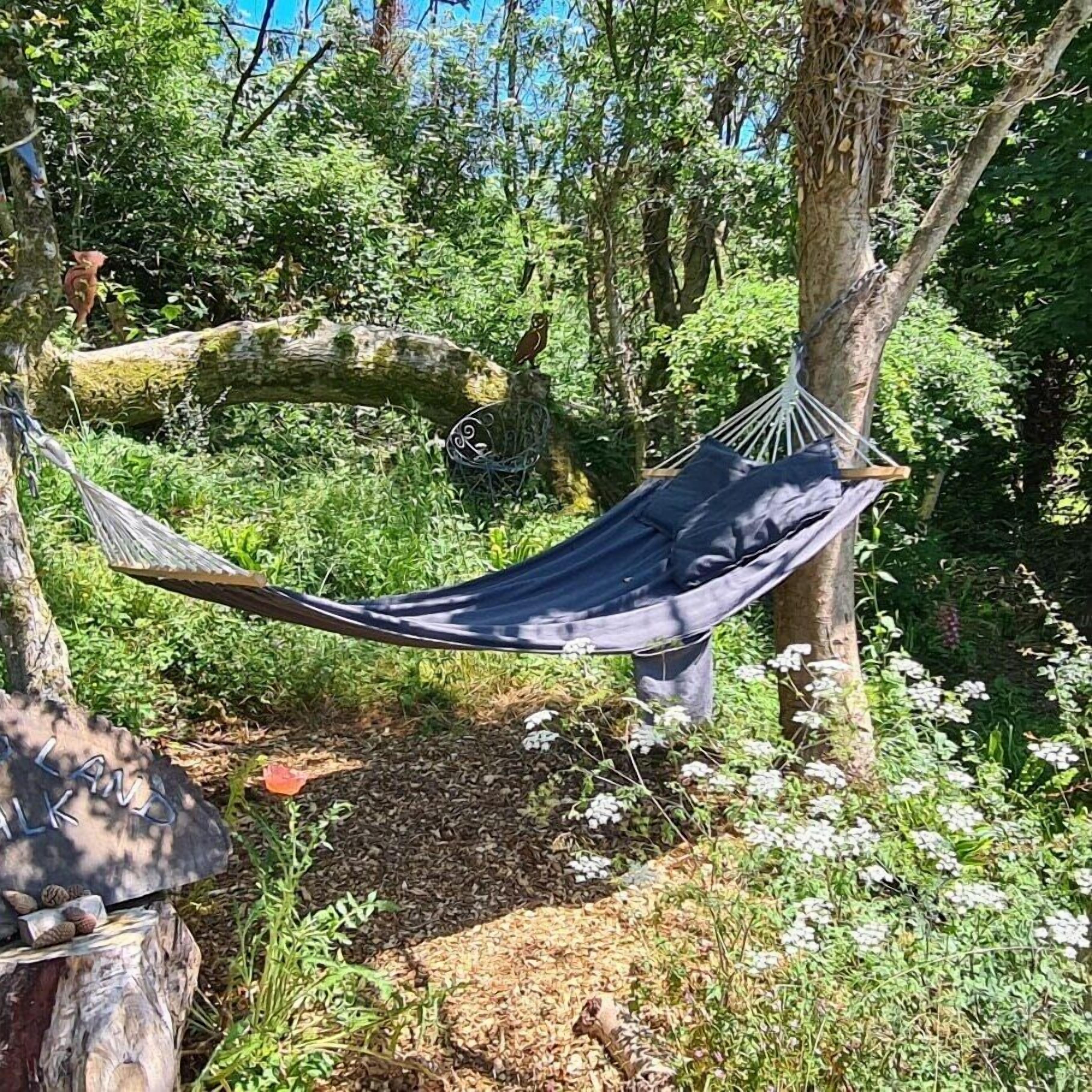 A hammock tied between trees in a forested area with a stone path and a wooden sign.