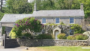 A stone house with a traditional design, featuring a stone wall, a wooden gate, and a well-maintained lawn.