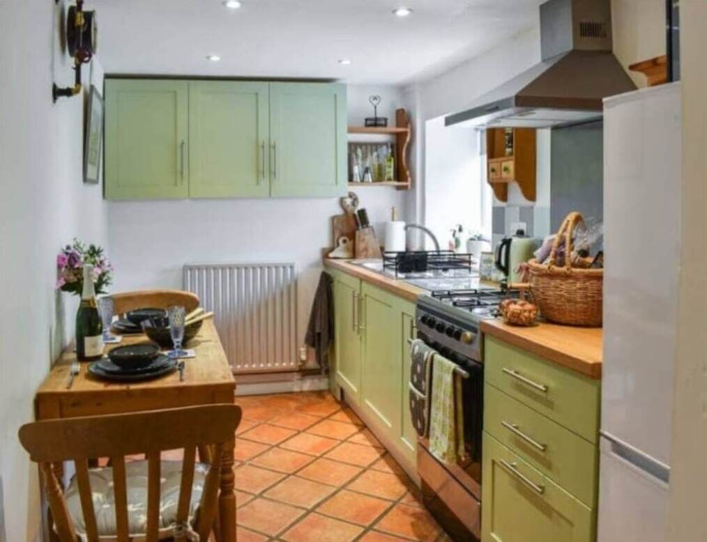 A compact kitchen with green cabinets, a wooden table, and a tiled floor.